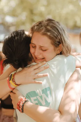 Due persone si stringono in un abbraccio: una tiene gli occhi chiusi e sorride commossa