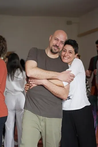 Due persone si abbracciano sorridendo, in una sala piena di gente