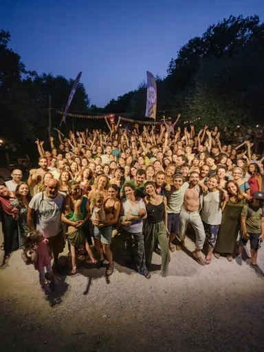 La foto di gruppo di sera: centinaia di persone del festival guardano verso chi scatta, molte con le braccia alzate
